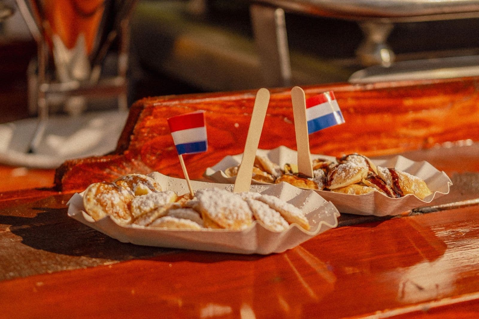 Twee bakjes verse poffertjes met poedersuiker en Nederlandse vlaggetjes op de houten toonbank van de kraam